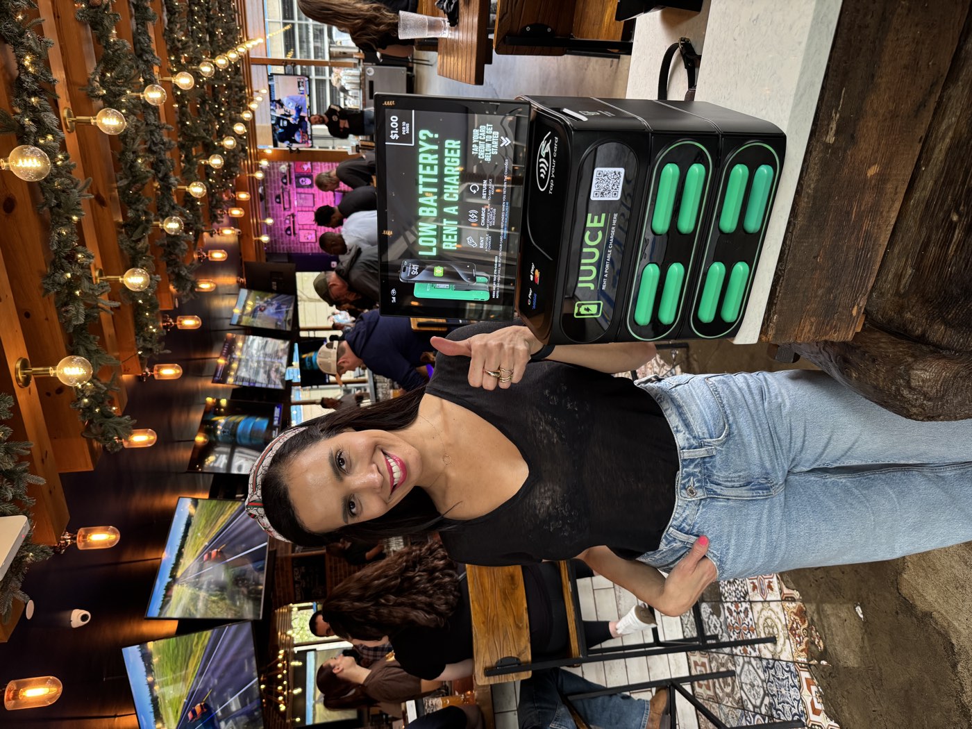 A smiling patron giving a thumbs-up beside a JUUCE station in a packed beer hall