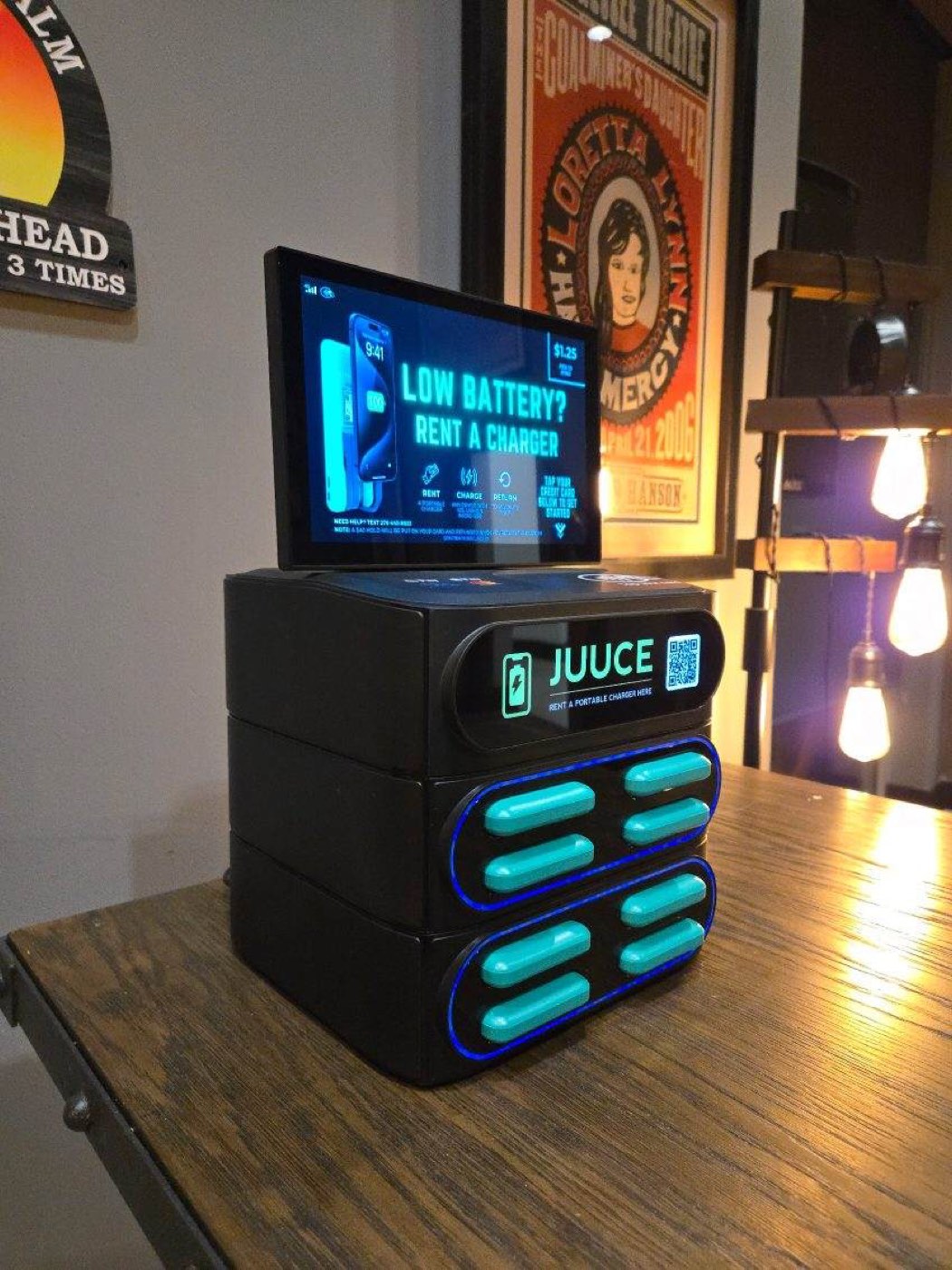 A fully stocked JUUCE station on a bar table, its screen reading "Low battery? Rent a charger"