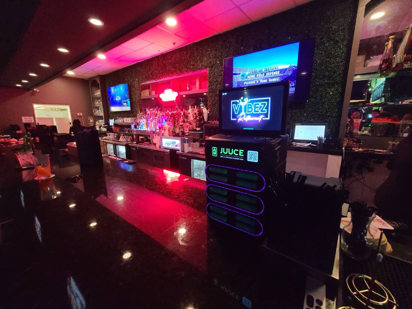 A JUUCE tower on the bar top at VYBEZ, chargers lit under the neon